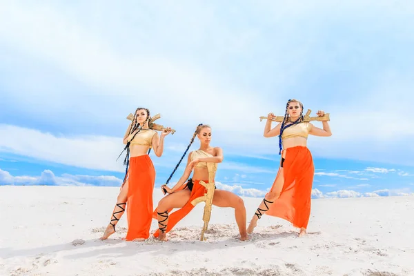 女孩们穿着红色的裙子 手里拿着金色的机器 在海滩上跳舞 白沙蓝天 — 图库照片