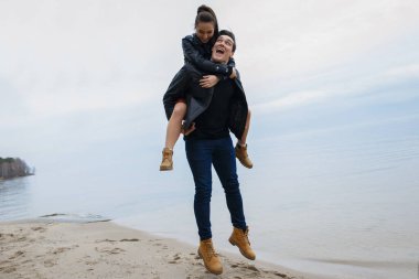 Siyah ceketli genç çift kumsalda sarılıp poz veriyorlar..