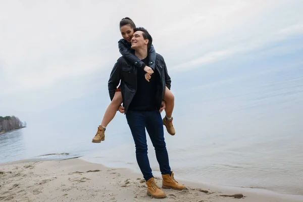 黒のジャケットを着た若いカップルがビーチで抱き合ってポーズをとって — ストック写真