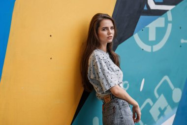 Şehirde mavi ve sarı çiçeklerden bir duvarın yanında poz veren bir kız.