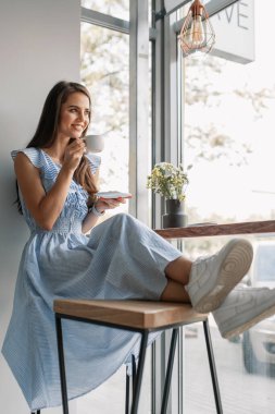 Kafede poz veren güzel bir genç kız. Elinde bir fincan kahve var.