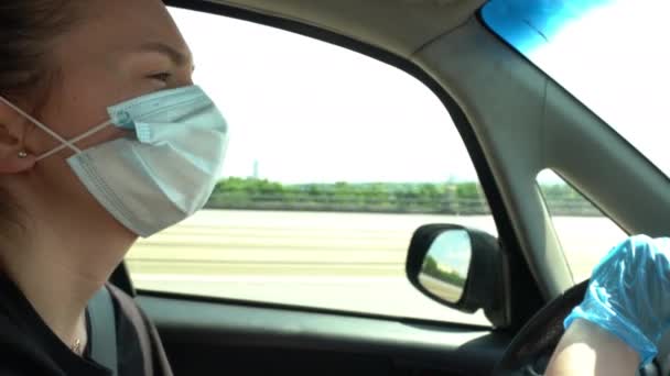 Νεαρή γυναίκα που οδηγεί με γάντια και μάσκα για την προστασία από τον ιό της στέψης — Αρχείο Βίντεο