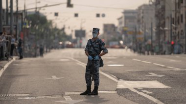Korumalı maskeli polis geçit töreninin önündeki meydanda duruyor.