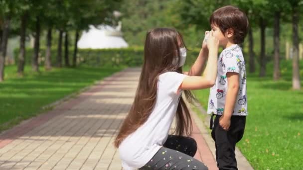 Una joven ayuda a su hermano a llevar una máscara facial del coronavirus covid19 — Vídeos de Stock