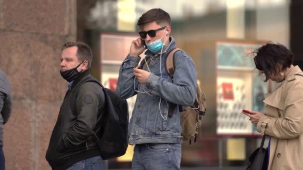 Хлопець у медичній масці з ковенірів стоїть у черзі і розмовляє по телефону. — стокове відео