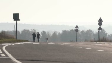 Banliyö otobanının kenarında yürüyen iki adamın silueti.