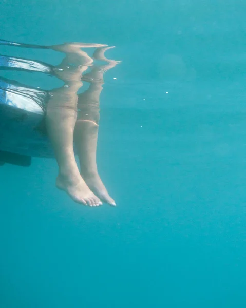 Underwater photo of two feet hanging down from a kayak. Stock photo of a person sitting in a kayak with her feet in the water shoot from below.