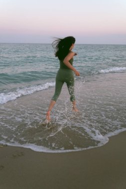 Gün batımında sahilde yoga yapan genç bir kadın. Akdeniz 'de egzersiz yapan bir kızın stok fotoğrafı..