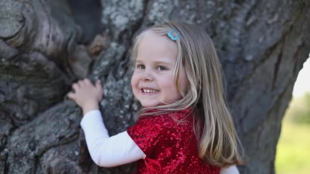 SLOW MOTION Happy cute bionda bambina in abito rosso toccare l'albero — Video Stock