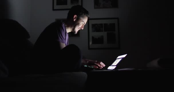 Brunette avec une barbe dans une pièce sombre imprime sur un ordinateur portable et se réjouit 