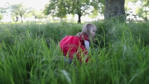 Glad liten flicka i röd klänning och hatt springa och ler i parken. Långsamma rörelser. — Stockvideo