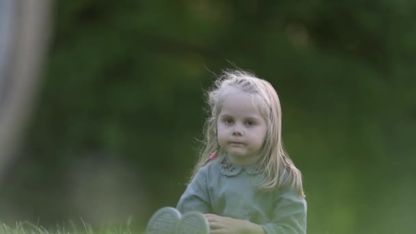 Pequeña niña linda sentada en la hierba a la hermosa luz del sol en verde — Vídeo de stock
