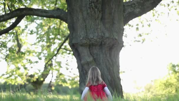 SLOW MOTION Glad söt blond liten flicka i röd klänning röra trädet — Stockvideo