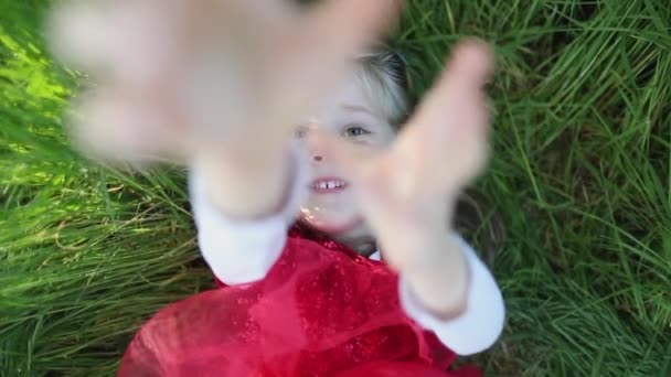 Glückliches kleines Mädchen in rotem Kleid lag im Gras und sagte Stopp. Zeitlupe. — Stockvideo