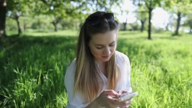 Sarışın anne açık havada telefonla konuşuyor. Çimlerde genç bir kadın