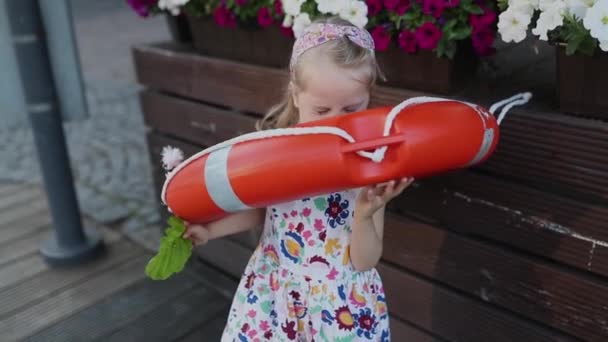 Niña rubia de pie cerca de la línea de vida. Flores en el fondo — Vídeos de Stock