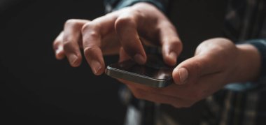 Adam cep telefonu kullanıyor, karanlık arka plan geniş görüntü. Telefona odaklan .