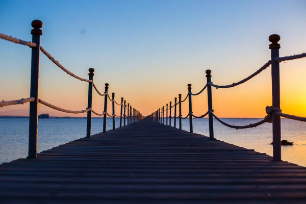 Primo piano di un ponte di legno scuro vicino al mare al tramonto arancione brillante, backgound, texture, carta da parati, incredibile vista romantica, un percorso per una nuova vita — Foto Stock