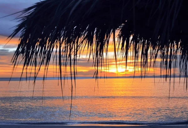 Vista da vicino dell'ombrellone di paglia al tramonto, spiaggia tropicale paradisiaca, nessuna gente, vista mozzafiato, tempo di vacanza, oceano sullo sfondo, cielo luminoso colorato — Foto Stock