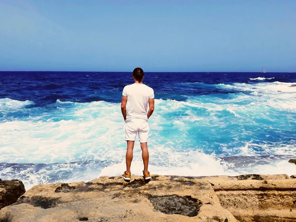 Przystojny młody mężczyzna w biały stojący na skraju skały z powrotem patrząc na fale morskie, Błękitne niebo, uspokoić, odkryty seksowna modelka, wierzą w nadziei, podróży turystycznych, zapraszam — Zdjęcie stockowe