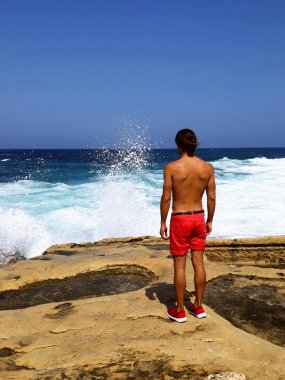 yakışıklı genç adam şortla tabaklanmış, rock ile denizde seyir arka kenarını kürsüye dalgalar, mavi gökyüzü, sakin ol, açık seksi manken, inanıyorum umuduyla seyahat turizm, özgürlük hissediyorum, sakin ol