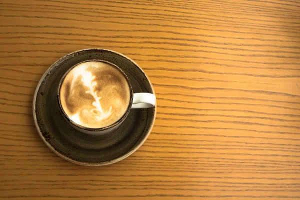 Zbliżenie na filiżankę cappuccino z piana projekt na żółty drewnianym stole w przytulnej kawiarni — Zdjęcie stockowe