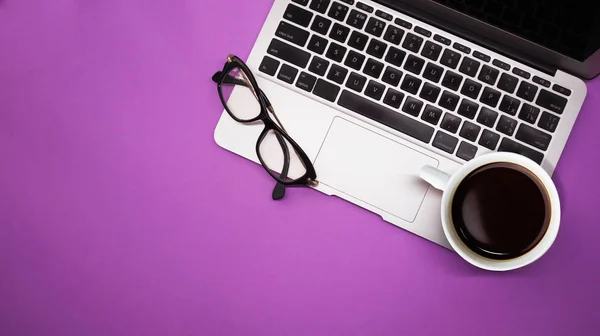 Szary laptop z filiżanką kawy i szklanki na fioletowym tle tabeli, miejsce pracy w domu lub w biurze Obrazek Stockowy