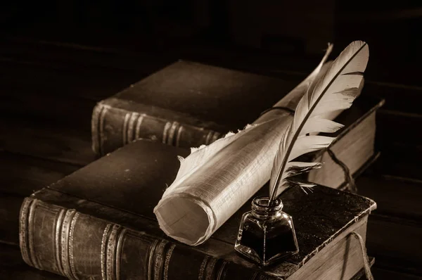 Red quill pen and a rolled papyrus sheet on a wooden table with old books, sepia effect