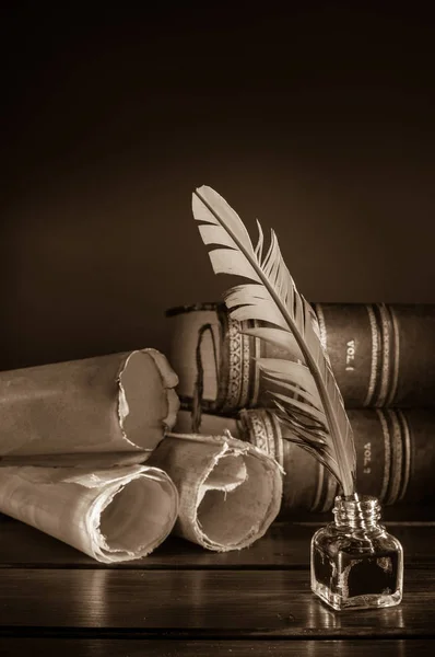 Quill pen and a rolled papyrus sheet on a wooden table with old books, sepia effect