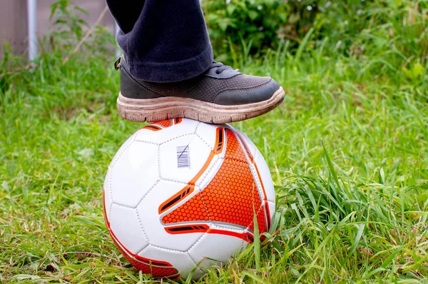 サッカーボールが草の上に立っているのではなく 白とオレンジのボールを持つ男の子の足 父の日 スポーツ家族の週末 — ストック写真