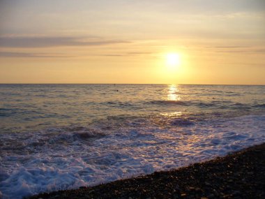 Gün batımında deniz kıyısında sörf yapmak. Akşam güneşinin arka planında deniz dalgalarının güzel manzarası. Gün batımında Hore. Güneşin arka planında deniz dalgalarının güzel manzarası.