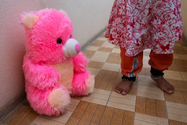 a close shot of pink teddy bear sitting on floor with baby girl legs background