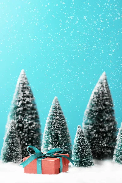 Kırmızı hediye kutusuyla Noel arkaplanı ve masasında bulanık Noel ağaçları.