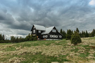 Ahşap evi ve arka planda bulutlu gökyüzü olan kırsal bir manzara. Ağaçlar ve tarlalarla çevrili bir çiftlik evi. Çek dağlarında yalnız bir turist evi. Sonbahar manzarası fotokopi alanı.