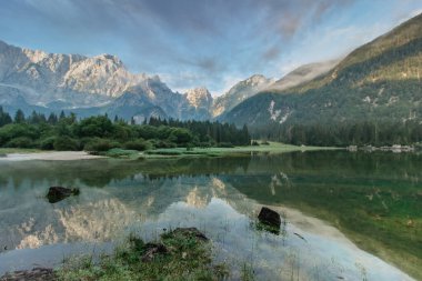 İtalya, Lago di Fusine 'de ayna yansıması. Yaz mevsimi renkleri ve arka planda Mangart dağı gün doğumunda Italien Alplerinde. Güzel huzurlu doğa manzarası, turkuaz su, seyahat arka planı..