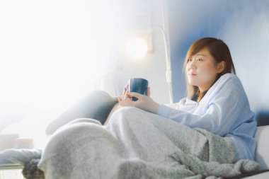 Genç ve güzel Asyalı kadın evde çalışıyor ve sıcak kahve içiyor. Mutlulukla evinde rahat bir odada.