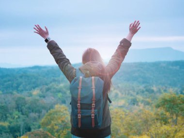 Sırt çantası ve kamp konsepti. Uzun saçlı, kalın giysili bir kadının sırt çantasından. Yolculuk, rahatlama, mutlu olma ve gün doğumundan sonra ormanı ve dağları görme.