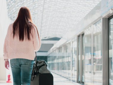 Seyahat ve aksesuar konsepti, kalın takım elbiseli güzel bir kadından modern tren istasyonu ve günışığı arka planına sahip bagaj koluna dokun ve it.