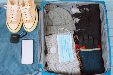 Koruyucu maskeli ve aksesuarlı üst manzara kış mevsimi için yeni normal tarzla seyahat için bagajda hazırlanıyor.