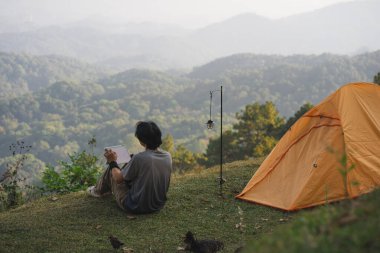 peyzaj ve seyahat konsepti yalnız başına çalışan bir adam tablet kullanır ve kedi ile oynar ve dağ katmanını görür.