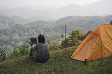 peyzaj ve seyahat konsepti yalnız başına çalışan bir adam tablet kullanır ve kedi ile oynar ve dağ katmanını görür.
