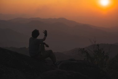 Tek başına serbest çalışan bir adamla manzara ve seyahat kavramı dağın tepesinde ve dağ katmanıyla gün batımında rahatlar.
