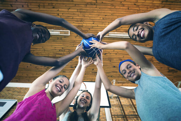 Низкий угол обзора улыбающихся старшеклассников, держащих баскетбол вместе на площадке
