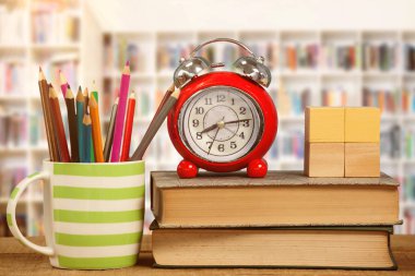 Çalar saat ve Öğretmen öğrencileri için kitap okuma karşı masada mug içinde renkli kalemler tarafından kitap