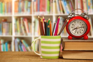 Çalar saat mug içinde renkli kalemler tarafından kitap kitap raf karşı masada