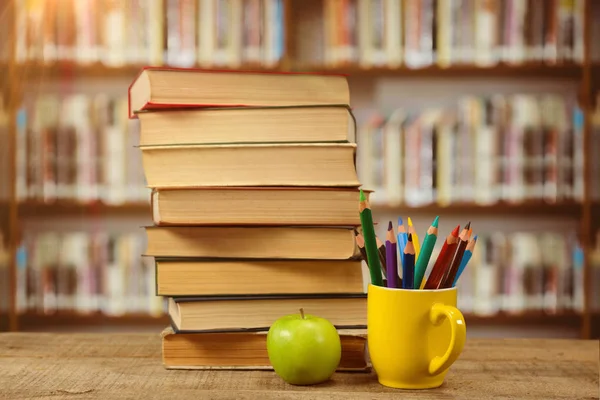 Bücherstapel Mit Buntstiften Becher Und Apfel Auf Tisch Gegen Bücherregal — Stockfoto