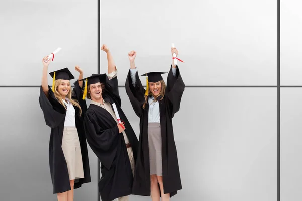 Three students in graduate robe raising their arms against white tiling