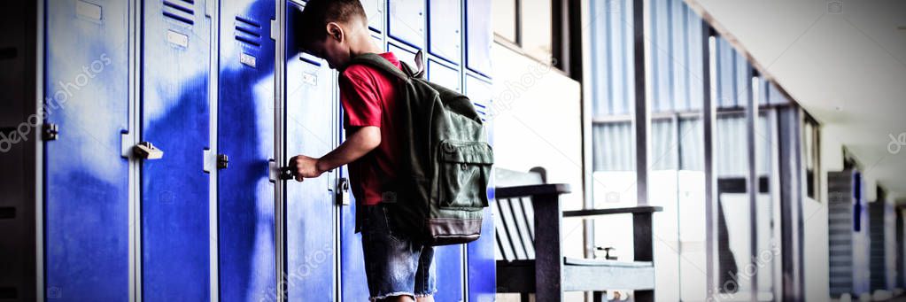 Full length of boy leaning on lockers in corridor at school