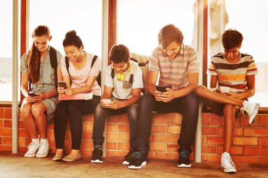 Pencere pervazına üzerinde oturan ve okulda koridorda cep telefonuyla mutlu öğrenciler