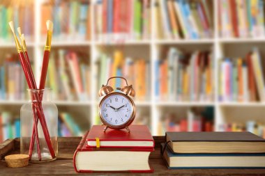 Boya fırçaları ve Kitaplar ile çalar saat ile kitaplar kitap raf karşı ahşap masa üzerinde